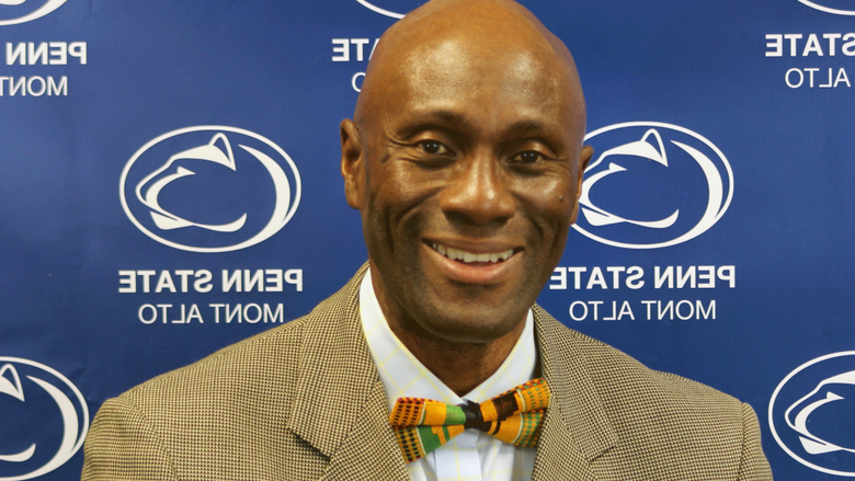 Photo of Francis Achampong in a tie and jacket in front of a blue Penn State backdrop. 